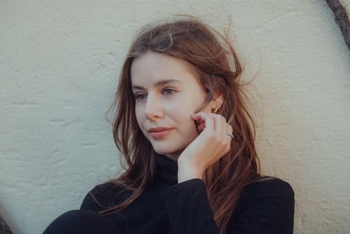 A woman with her earphones on leaning against a wall