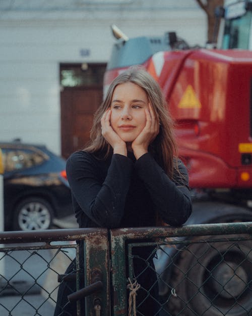 A woman leaning against a fence with a red truck in the background