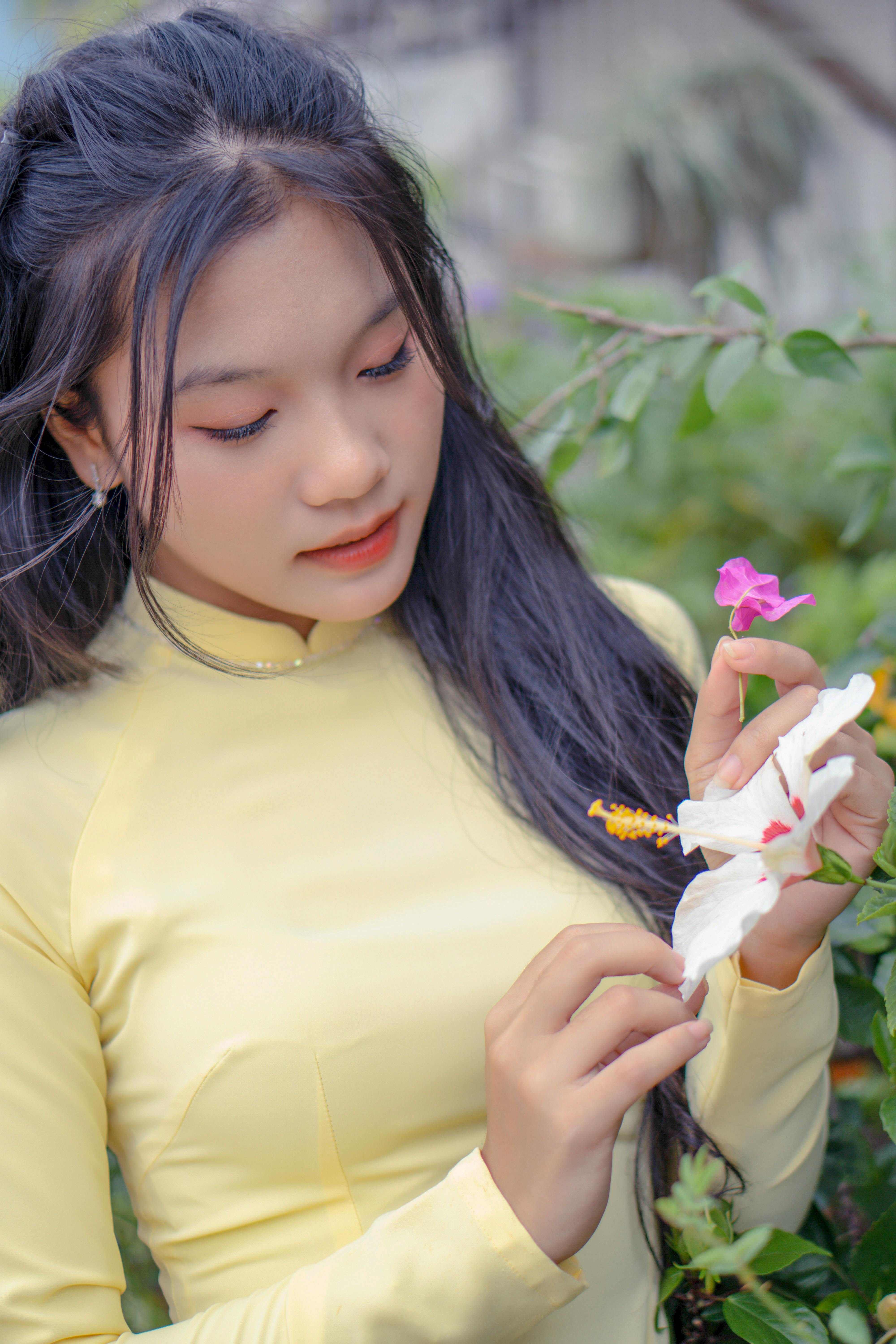 Portrait of a young woman in a yellow tunic holding flowers outdoors in natural light.