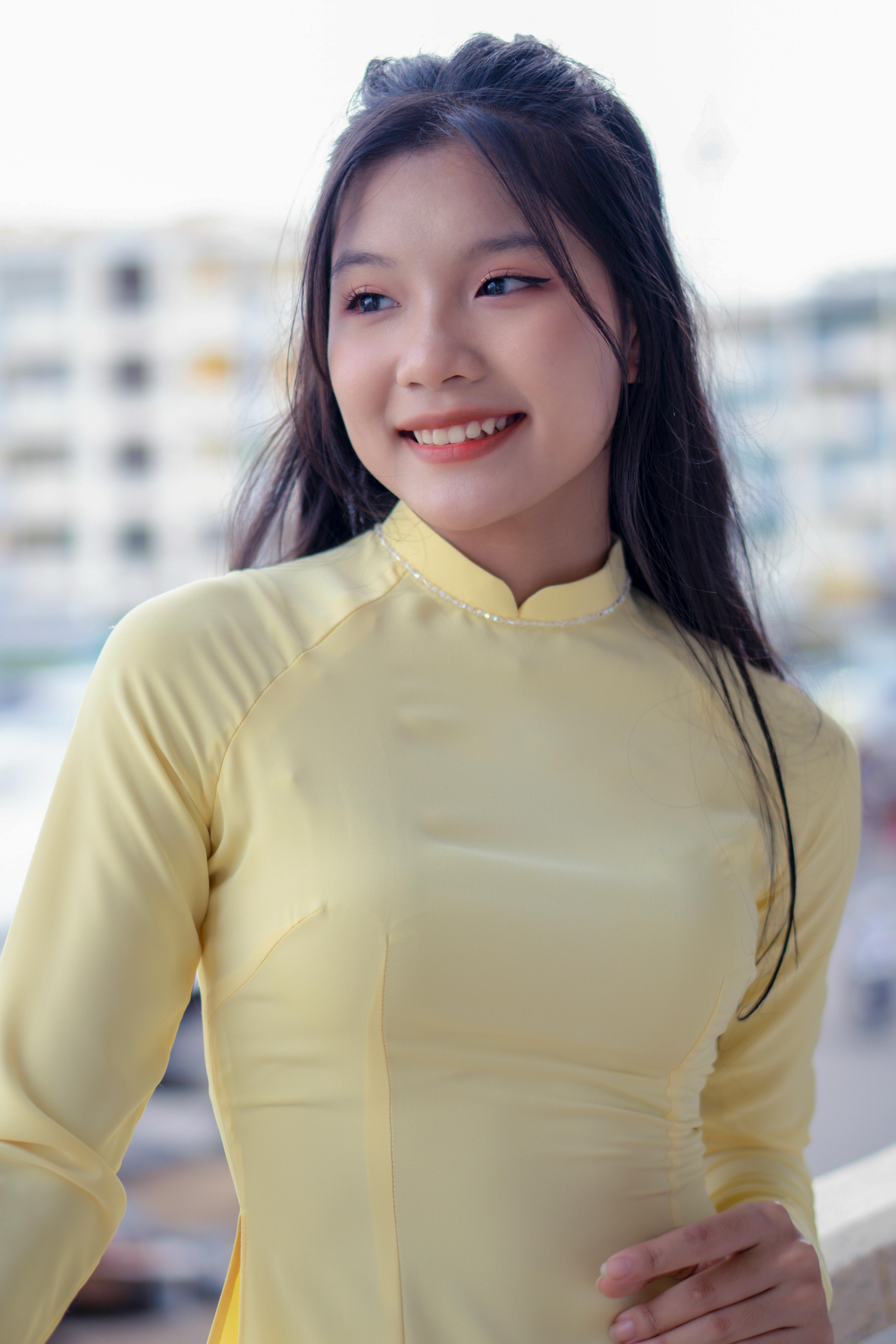 A cheerful young woman poses in a yellow traditional dress in an urban outdoor setting.
