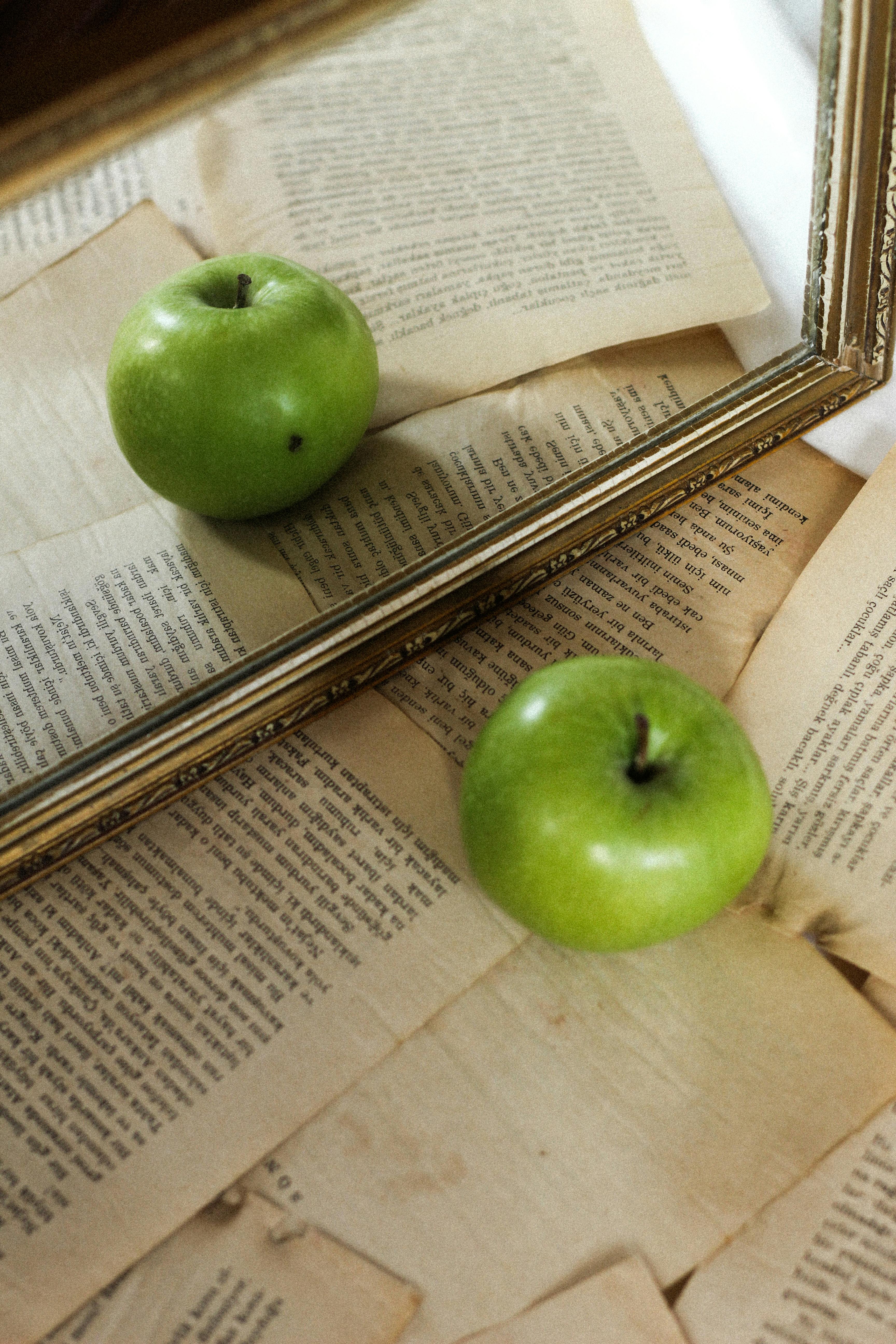 Green Apple on Old Book Pages Reflected in a Mirror · Free Stock Photo