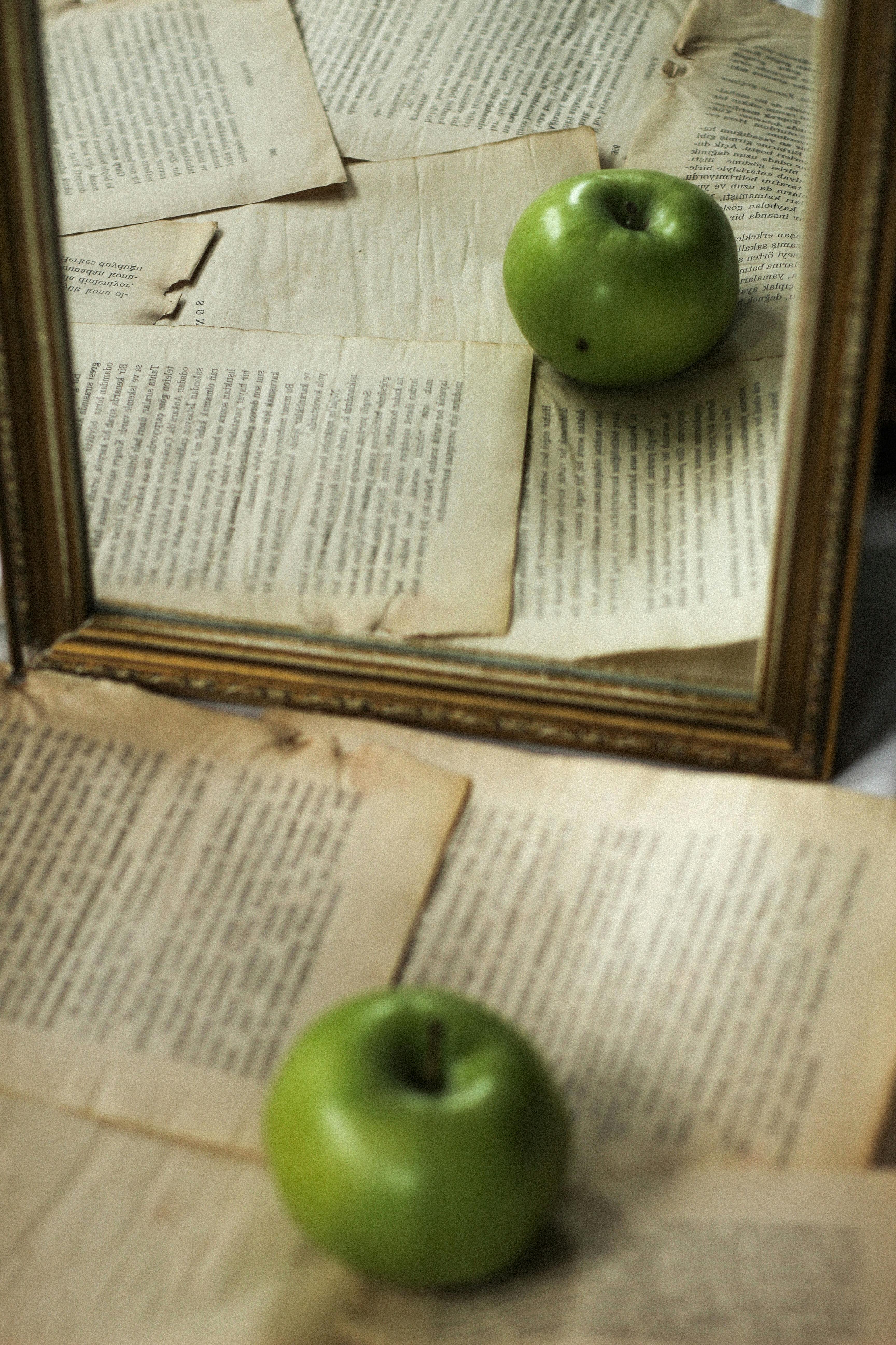 Green Apple on Old Book Pages Reflected in a Mirror · Free Stock Photo