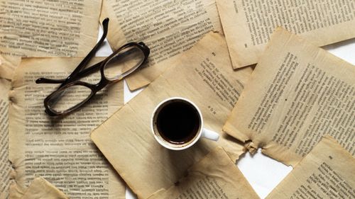 Free A flat lay of coffee, eyeglasses, and aged book pages for a vintage feel. Stock Photo