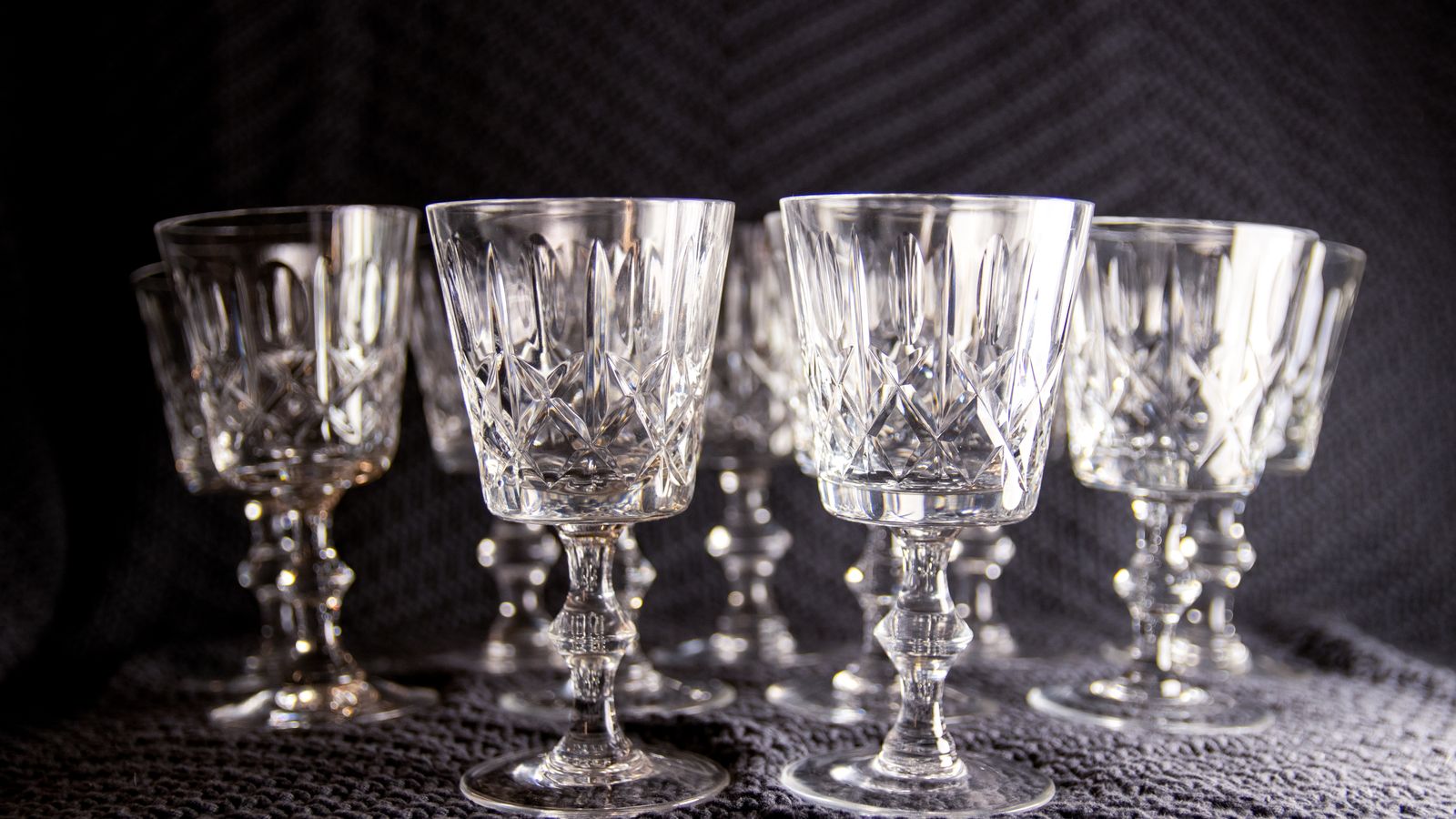 A set of cut-crystal goblets standing on textured fabric under soft light