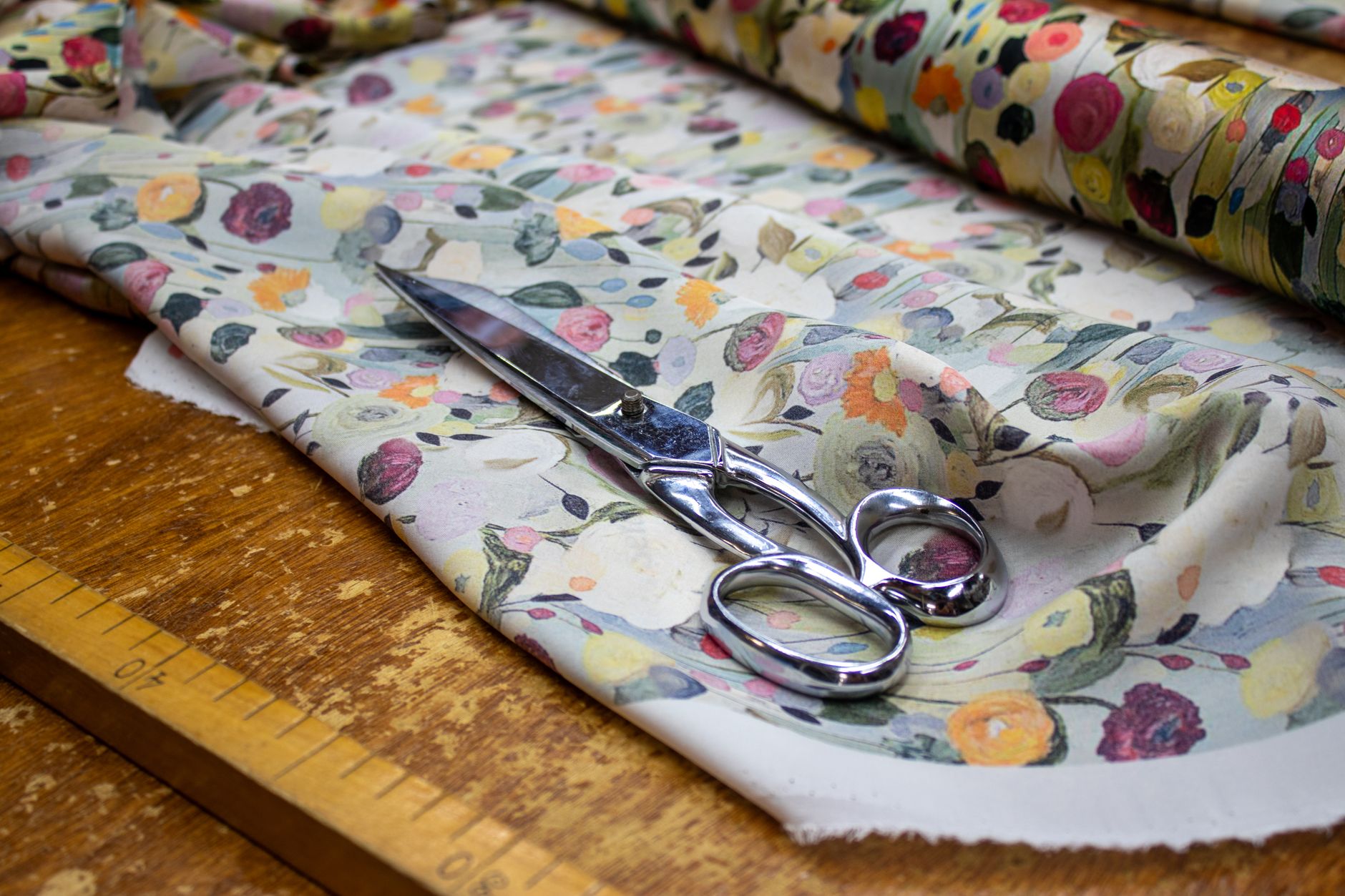 Elegant floral fabric with scissors and a ruler on a wooden table, ready for sewing.