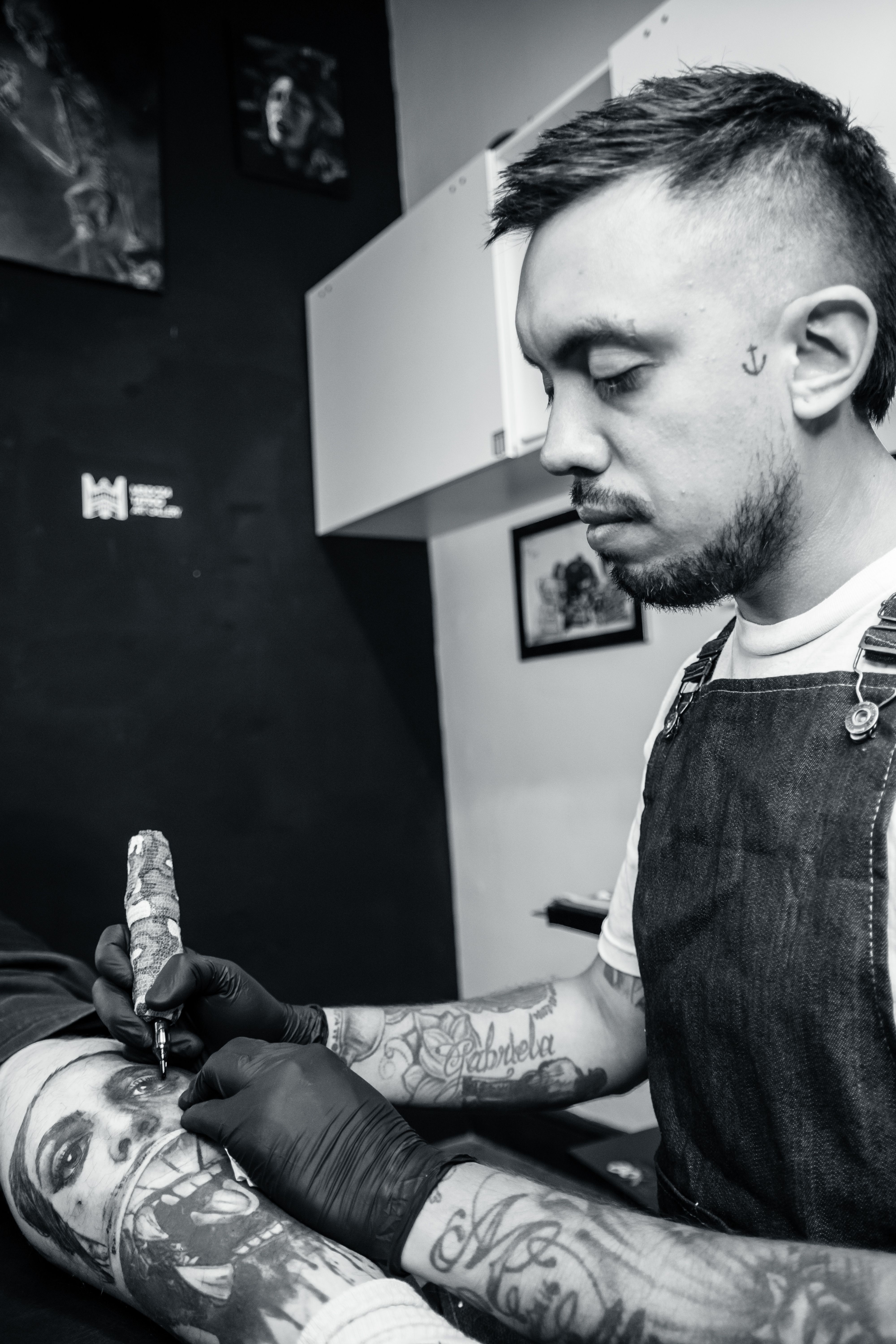 Tattoo artist focused on crafting a detailed black and white tattoo in a studio setting.