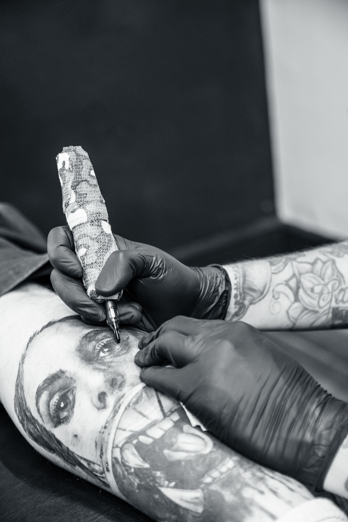 Artist tattooing a portrait piece in black and grey
