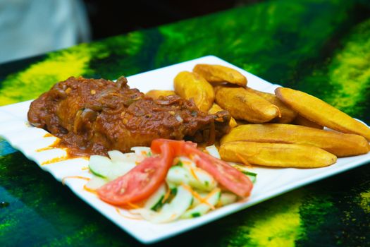 A vibrant plate of fried plantains with a savory tomato-based sauce and fresh salad.
