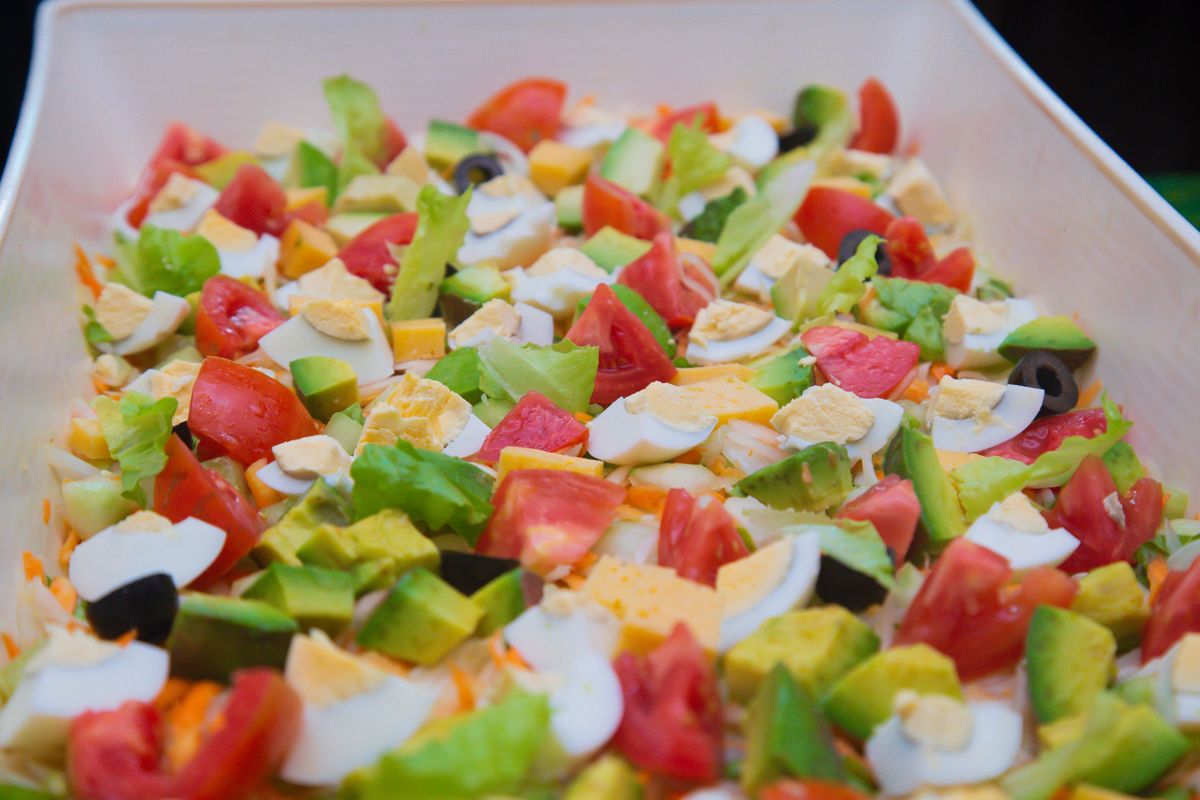 Chopped salad of tomatoes, avocado, boiled egg, cheese cubes, olives and lettuce in white dish