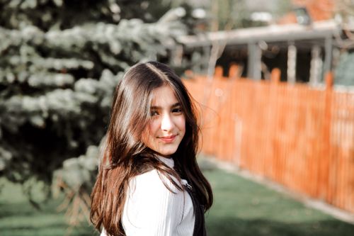 Free Portrait of a smiling teenager with long brown hair standing outdoors in a sunny garden. Stock Photo