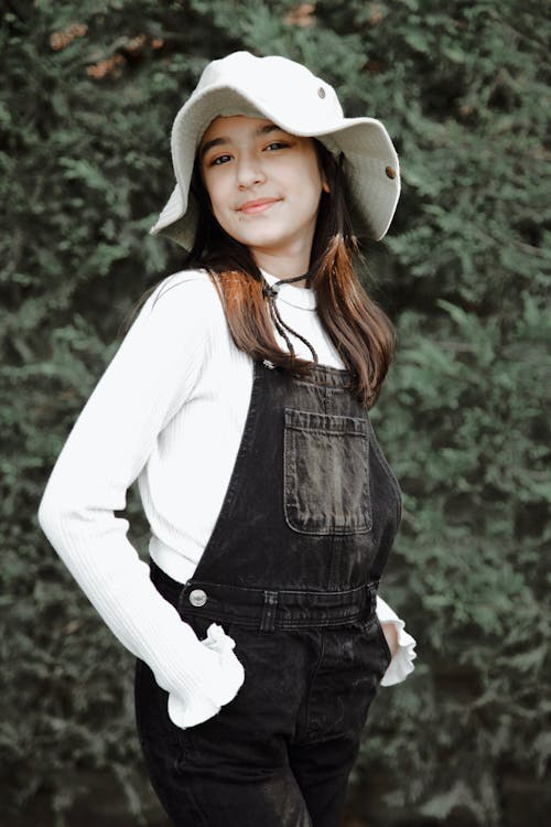 A girl in overalls and a hat posing for a photo