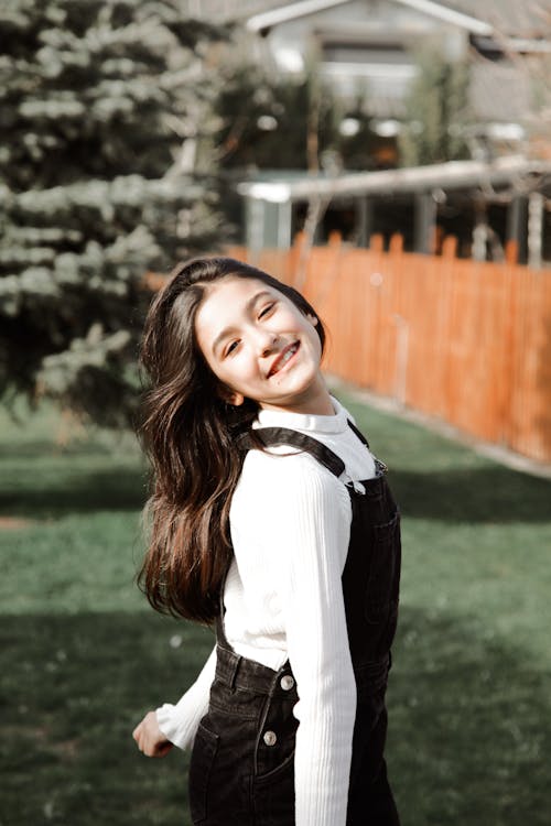 A girl in overalls smiling in the grass