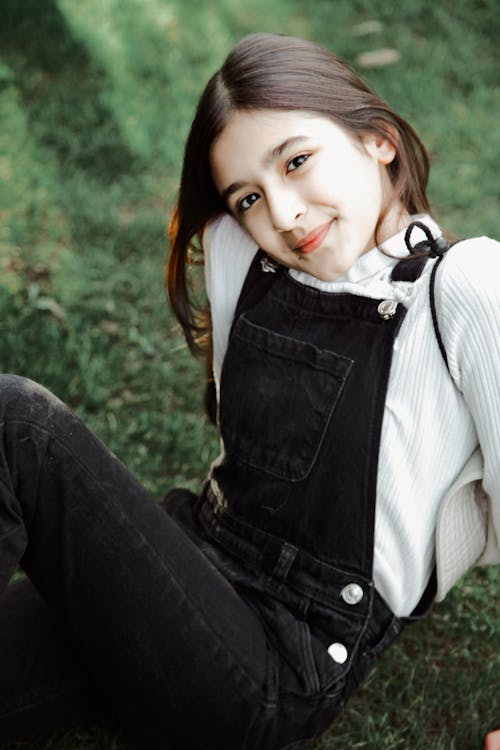 A girl in overalls sitting on the grass