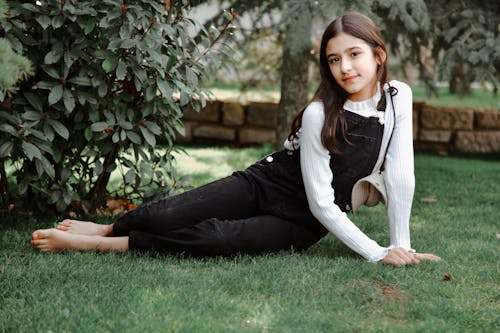 A girl laying on the grass in a black overalls