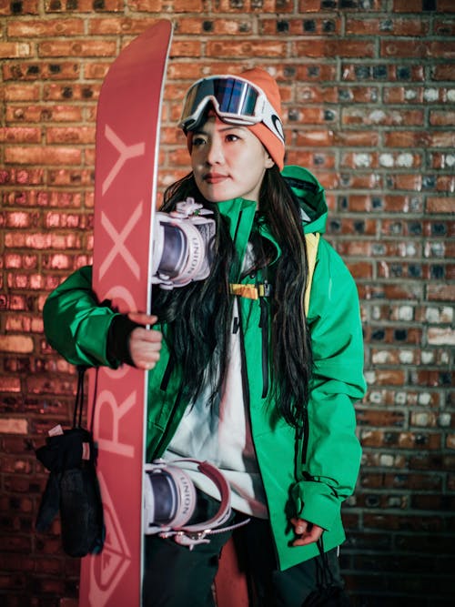 A young woman in green jacket holding a snowboard