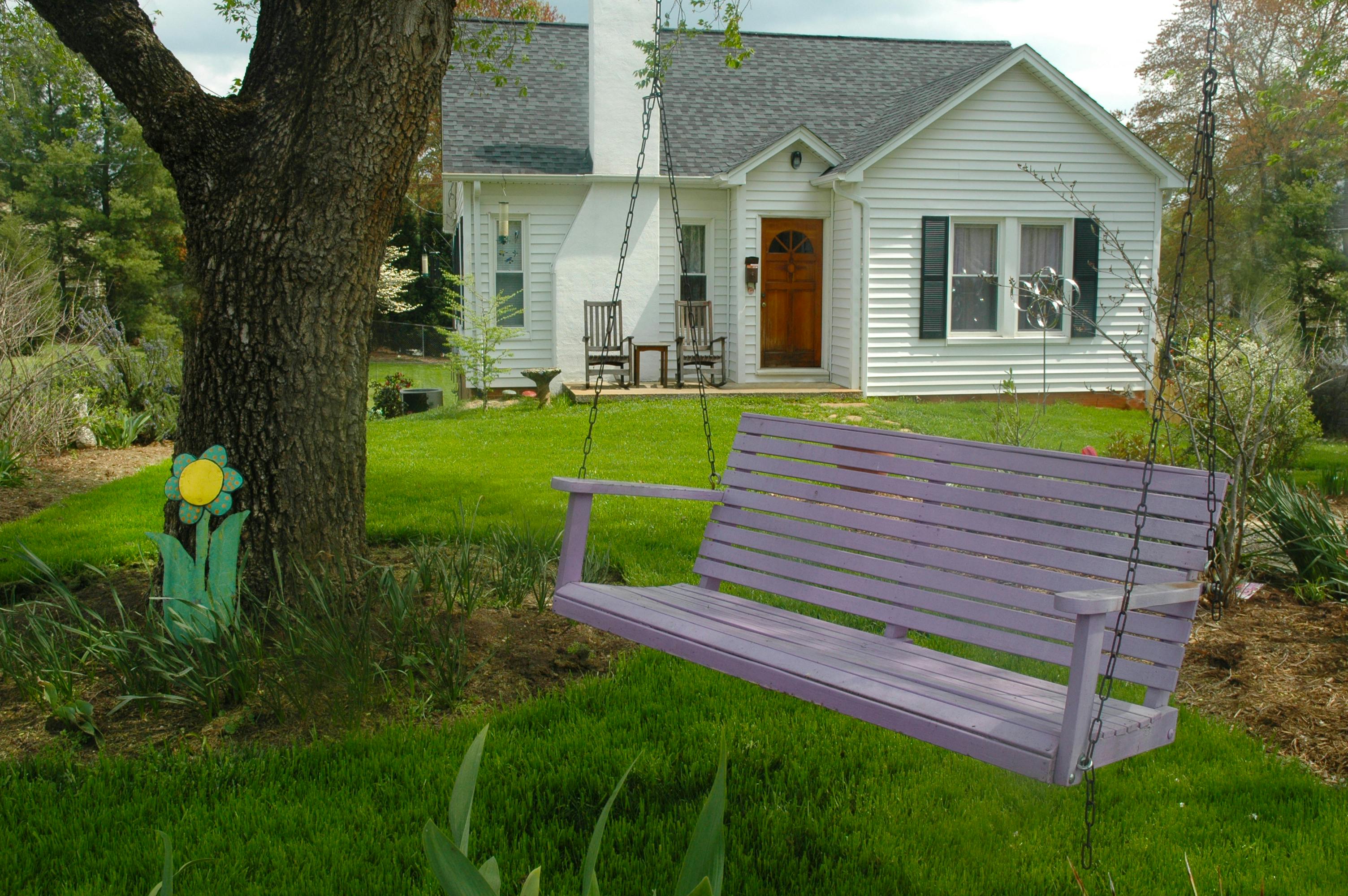 A quaint house with a purple swing bench in a lush garden, perfect for countryside relaxation.