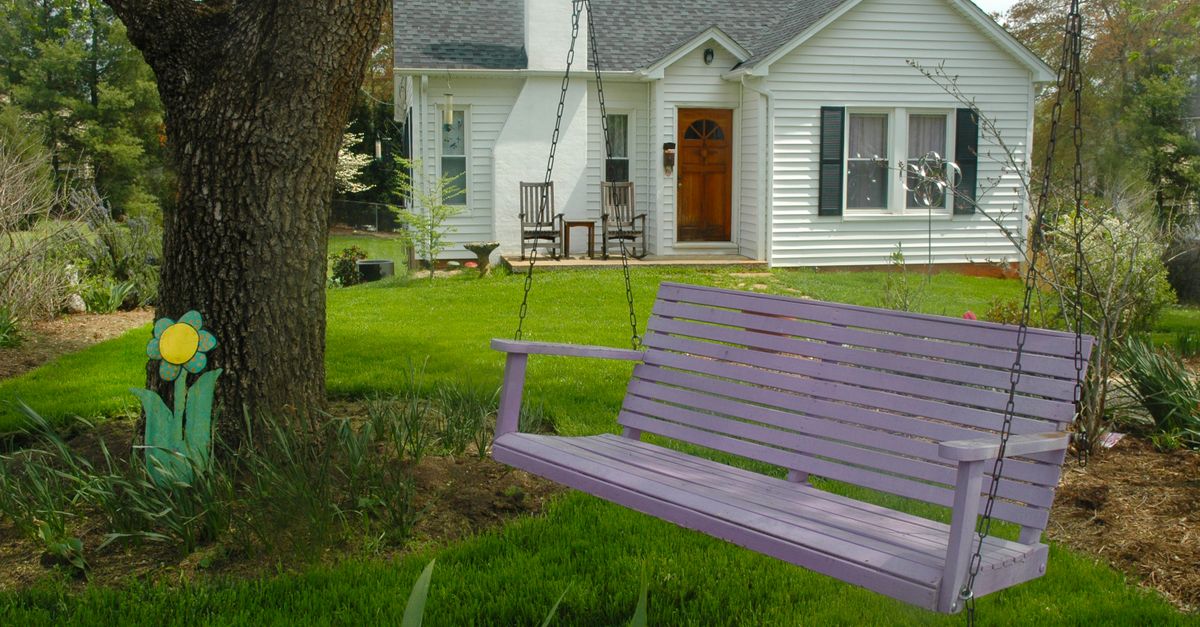 A quaint house with a purple swing bench in a lush garden, perfect for countryside relaxation.