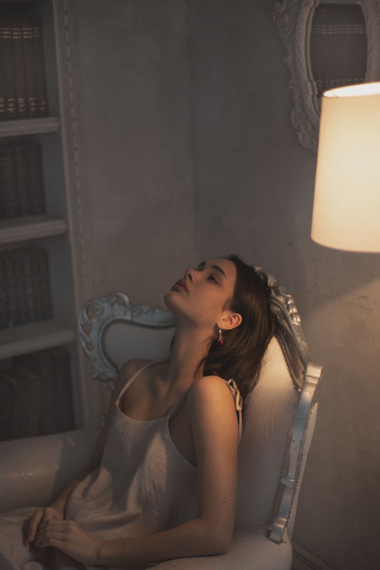 Young Woman In Dress Sitting On Armchair Next To Lamp