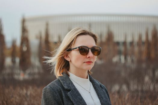 Portrait of a woman in sunglasses and gray jacket, set against an outdoor background.