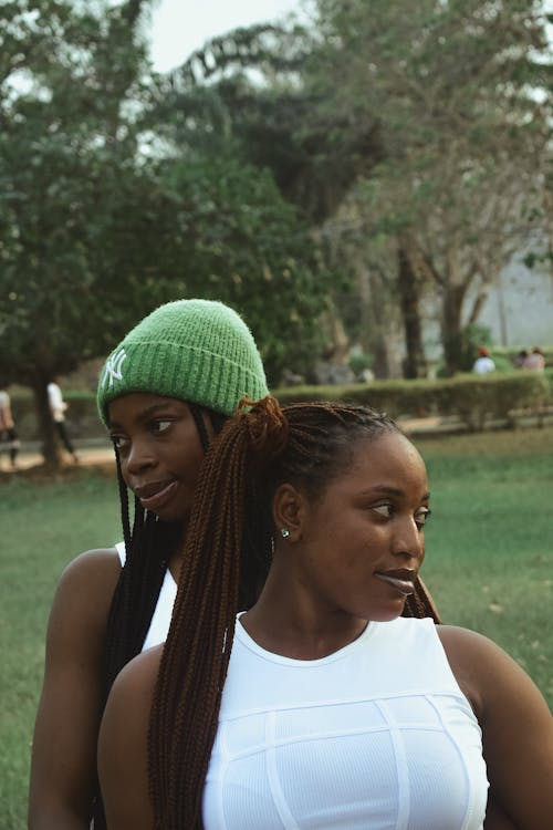 Two women in white tops and green beanies standing in a park