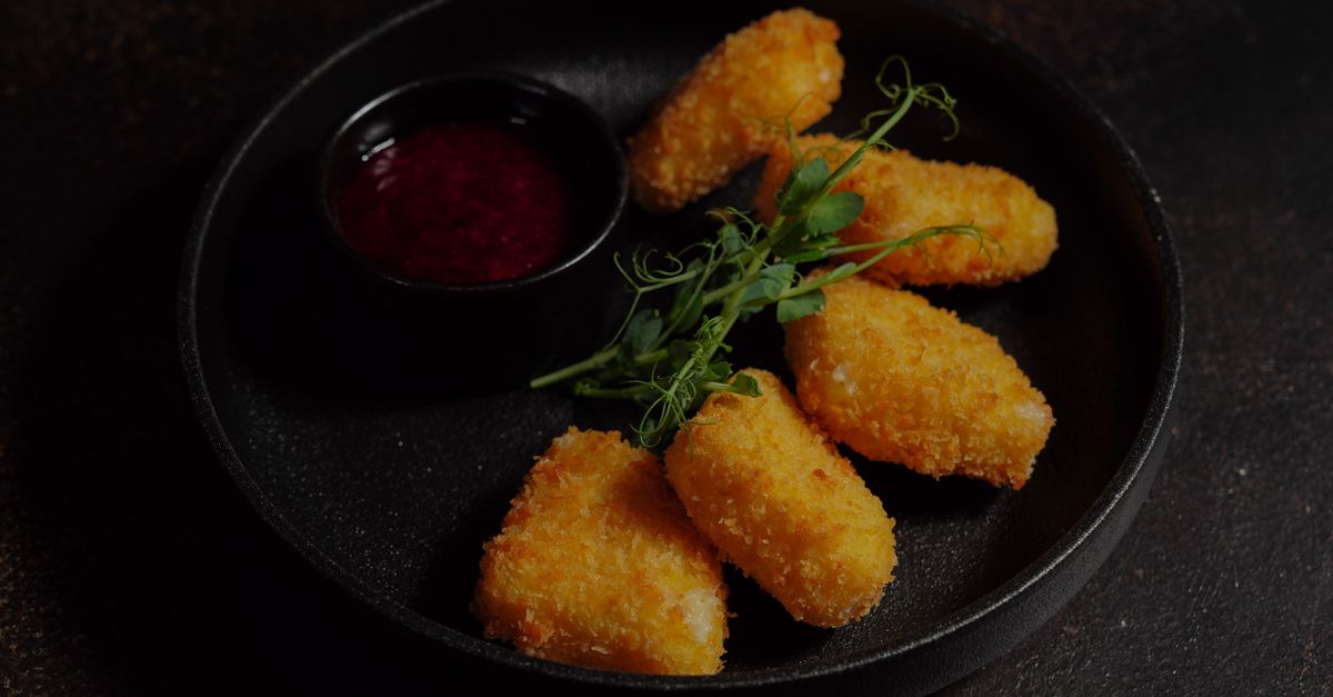 Deliciosos nuggets de frango crocantes servidos com um molho picante em um prato preto.