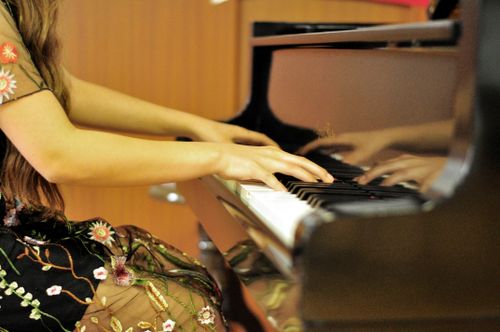 Free Hands of a woman gracefully playing the piano in a floral dress indoors. Stock Photo