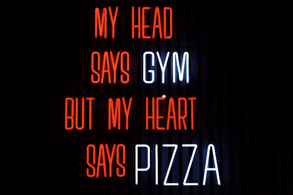 Colorful neon sign humorously declares 'My head says gym but my heart says pizza' in Jönköping, Sweden.