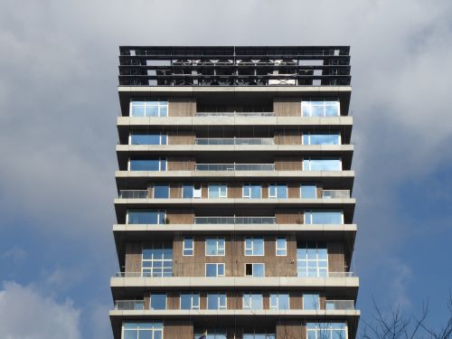 Free A modern high-rise building with a sleek glass facade under a cloudy sky. Stock Photo