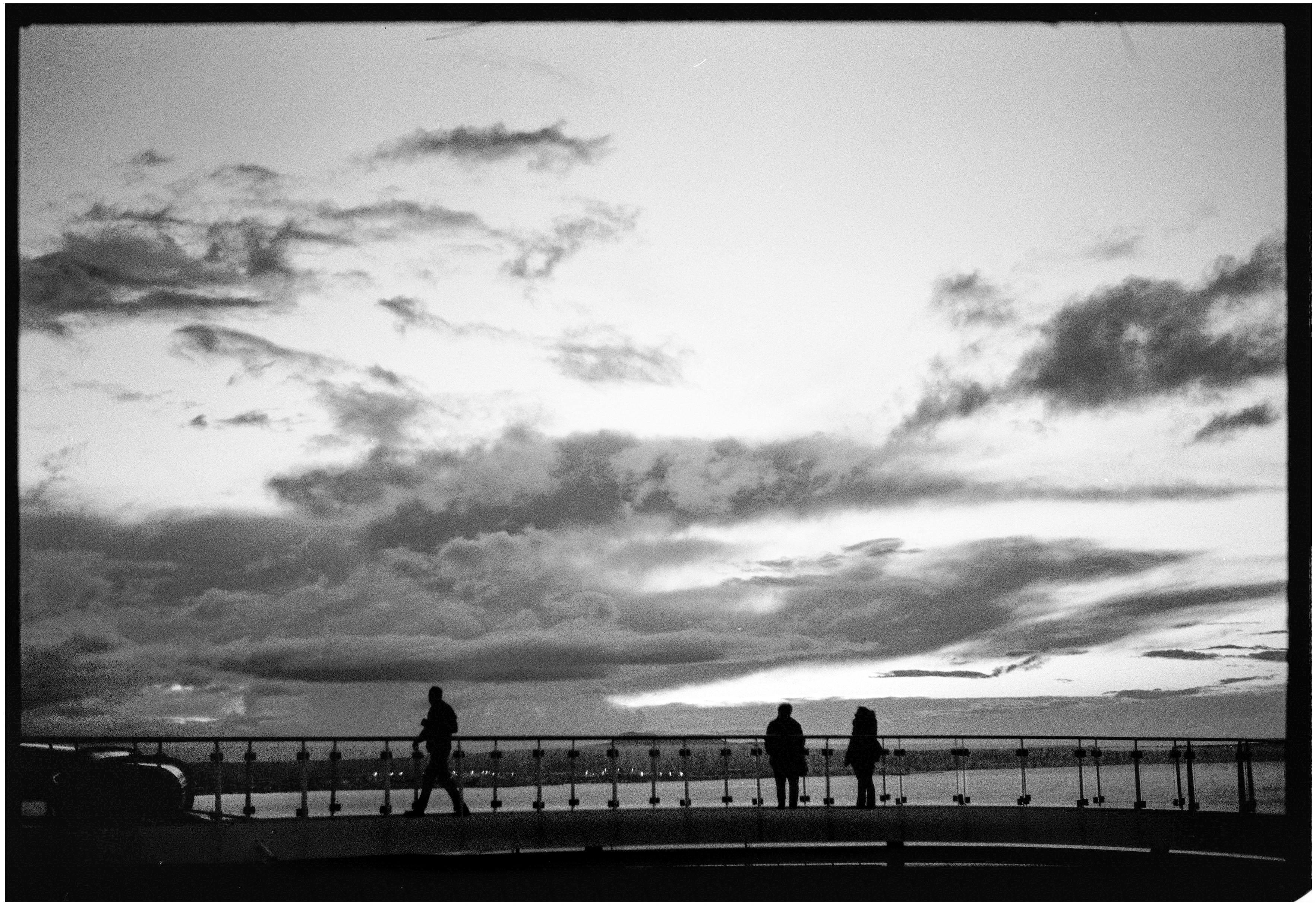 A serene black and white scene of silhouettes against a dramatic evening sky on a coastal walkway.