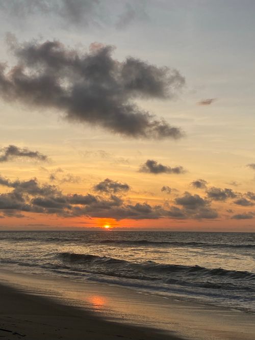 Free Peaceful beach sunset with clouds reflecting over calm ocean waves. Stock Photo