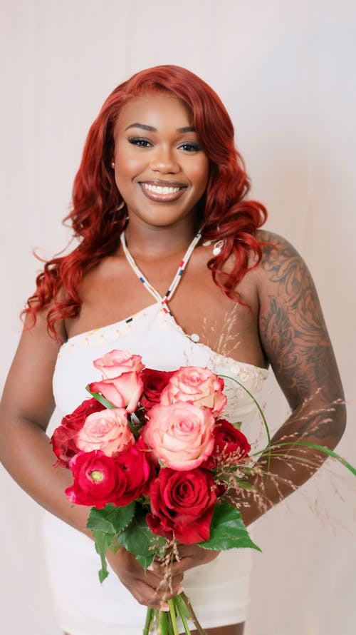 A woman with red hair and a white dress holding a bouquet