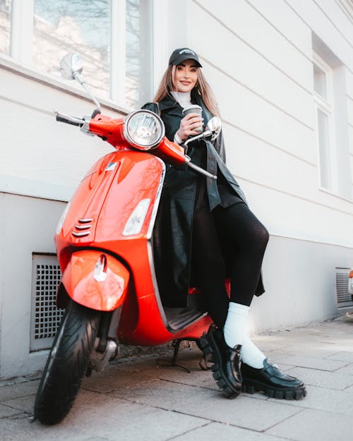 A woman in black and white sitting on a red vespa