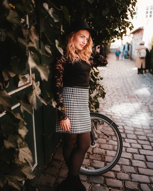 A woman in a black top and skirt posing near a bike