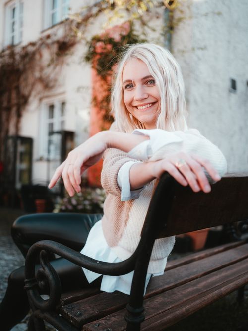 Free Blonde woman smiling while sitting on a wooden bench in a city environment, showcasing urban lifestyle. Stock Photo