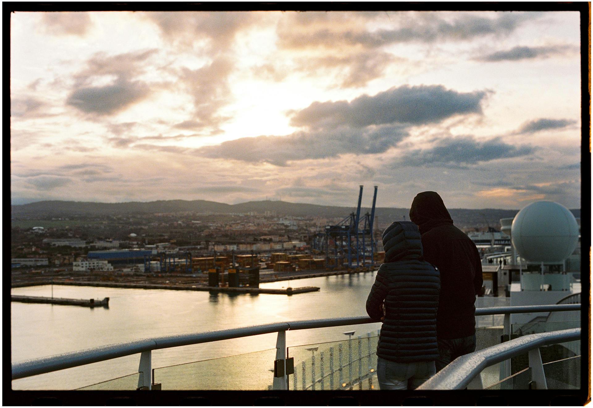Tourists view the Civitavecchia port skyline at sunset, capturing a moment of urban tranquility.