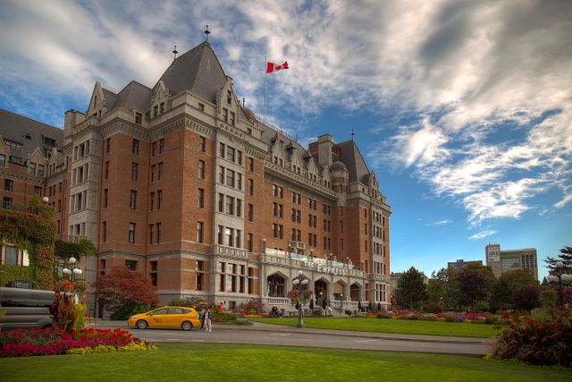 Historic Empress Hotel in Victoria, Canada under vibrant blue sky with colorful gardens and Canadian flag. Related image for Hospitality in Canada: What Comes Next for Modern Properties.