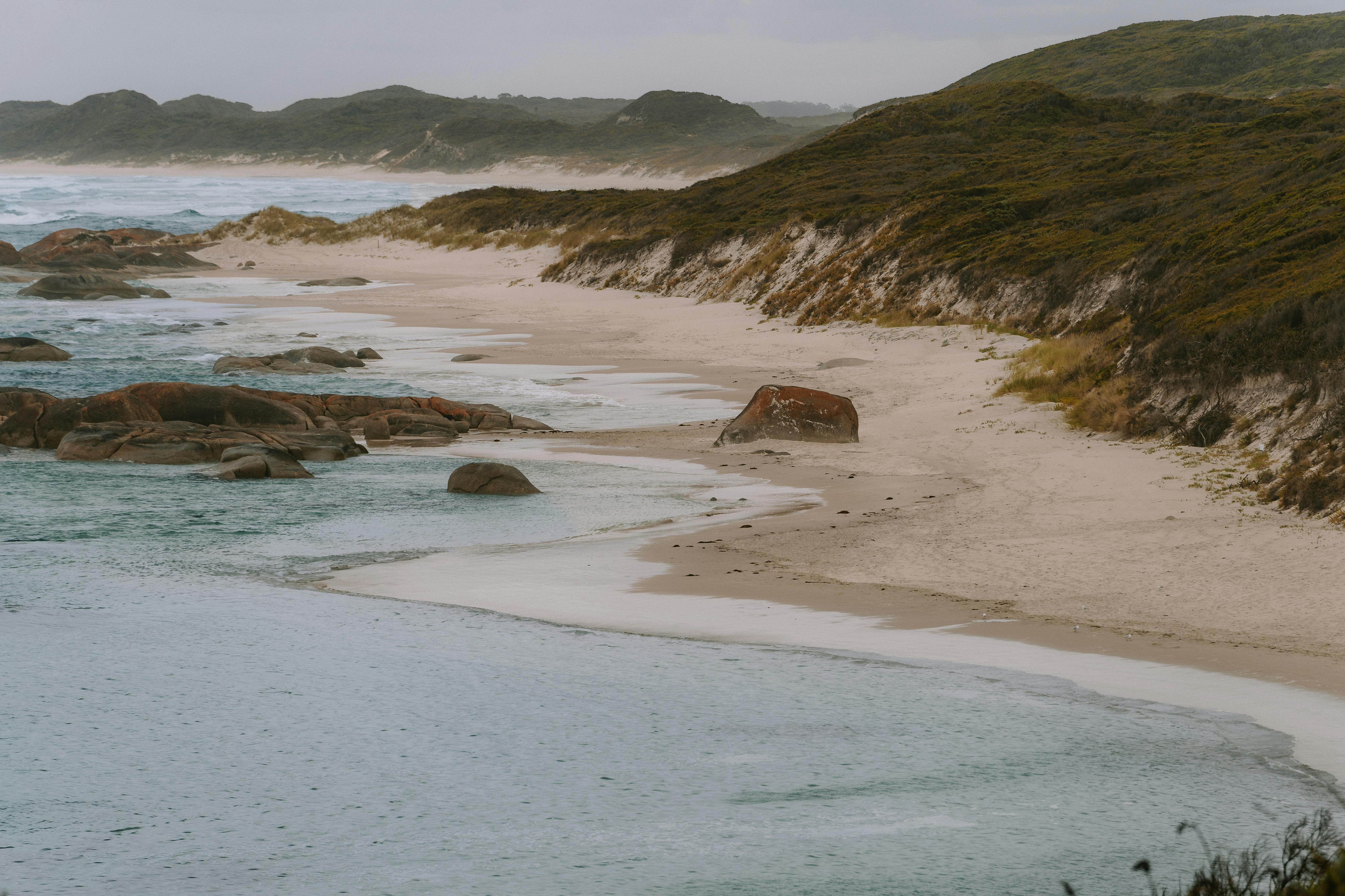 Peaceful view of Yallingup Beach with rolling waves, rocky shore, and misty hills in Western Australia.
