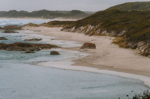 Free Peaceful view of Yallingup Beach with rolling waves, rocky shore, and misty hills in Western Australia. Stock Photo