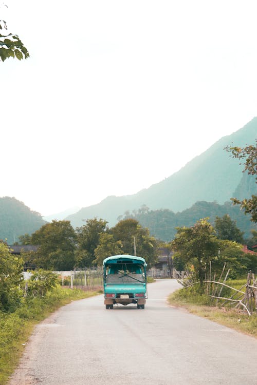 A small truck driving down a road with mountains in the background