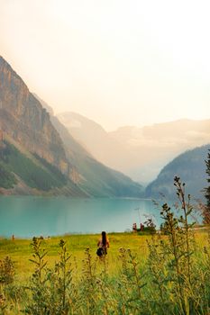 A tranquil scene of a lake surrounded by misty mountains and grassy fields at sunset.