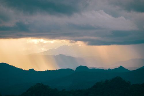 Free A breathtaking view of sun rays piercing through clouds over misty mountains at sunset. Stock Photo