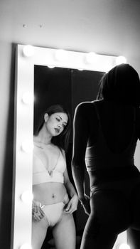 Artistic black and white portrait of a woman in front of a mirror, capturing reflection.