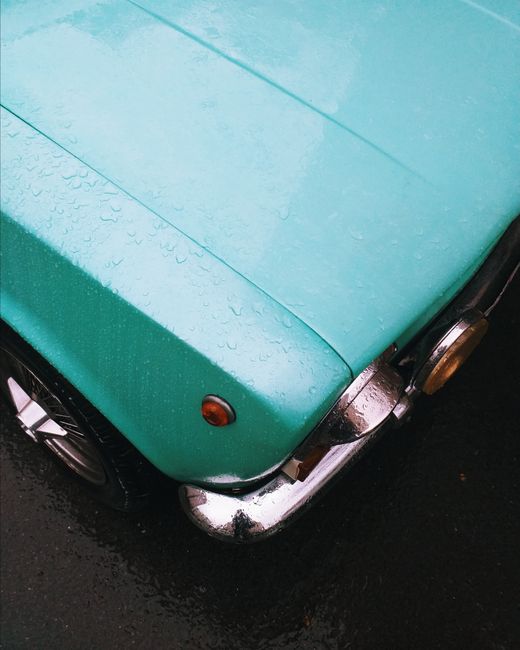 Close-up view of a vintage turquoise car hood with raindrops, showcasing retro design and chrome detailing.