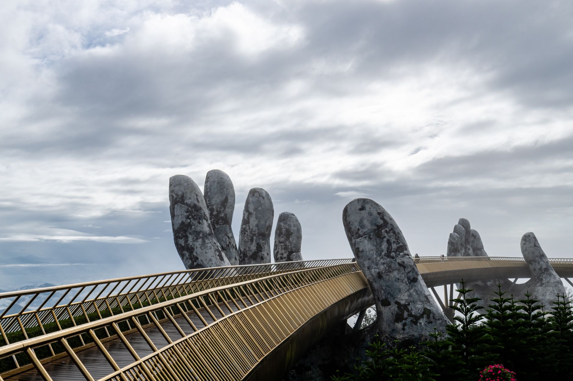 Photograph of the iconic Golden Bridge with hand sculptures in Da Nang, Vietnam under a cloudy sky.