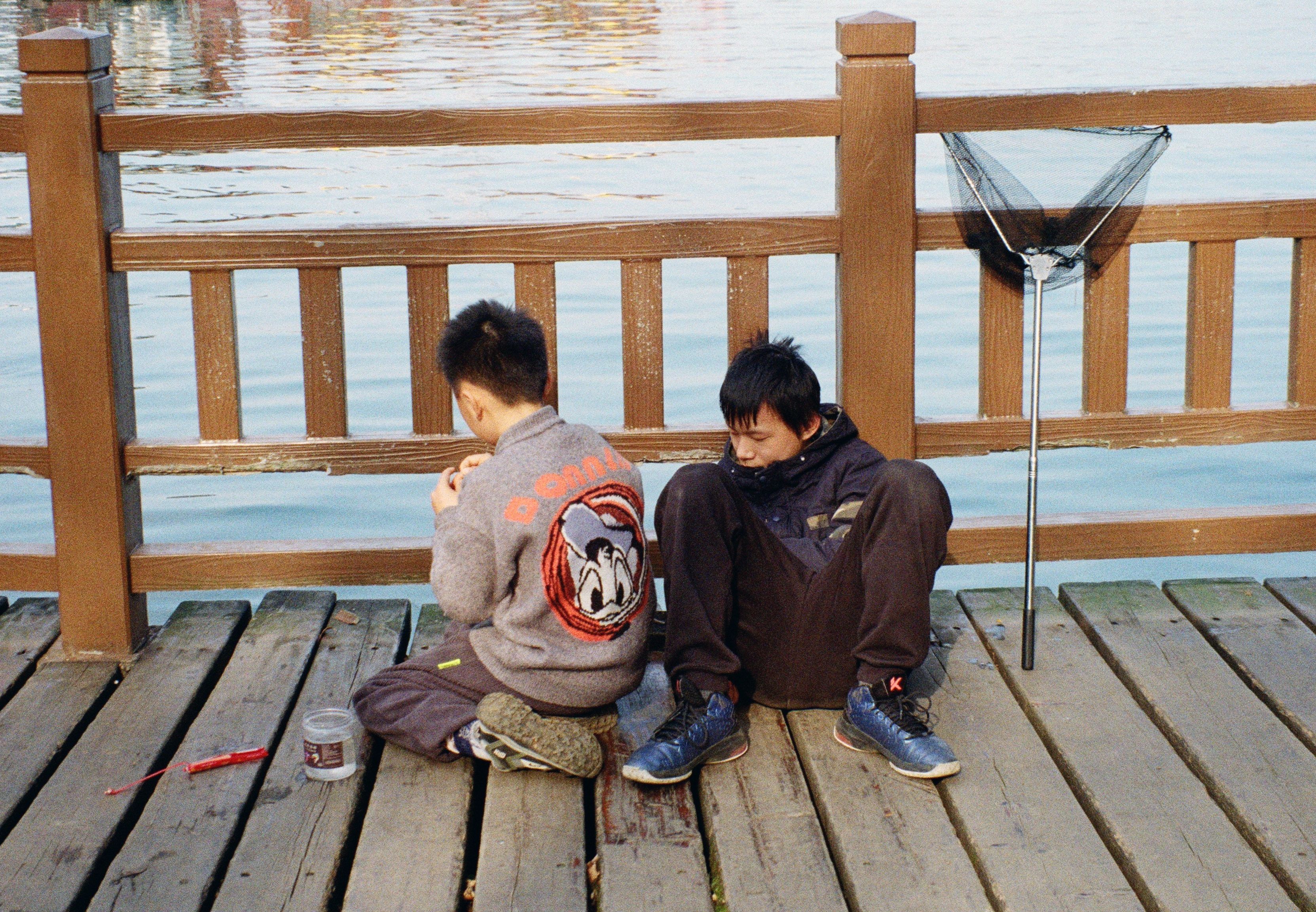 Two boys fishing on a wooden pier by the lake, enjoying a quiet day outdoors.