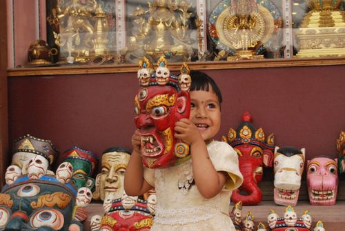 Free Young girl holds a vibrant cultural mask in a souvenir shop in Kathmandu, Nepal, surrounded by colourful sculptures. Stock Photo