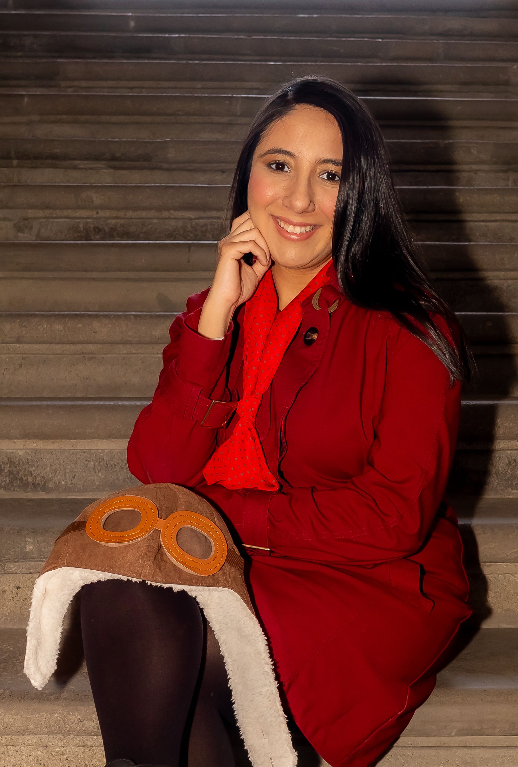 A woman in a red coat smiling while sitting on stairs in Mexico City. Fashionable and warm atmosphere.