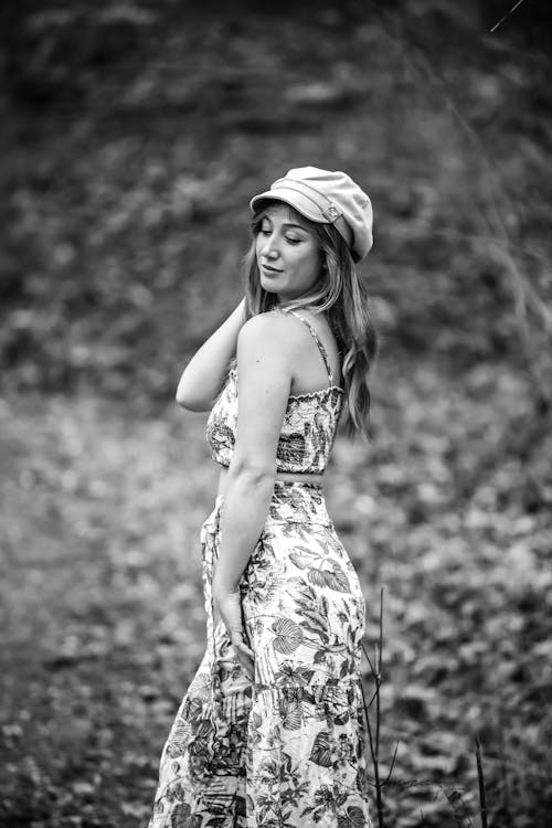 A woman in a floral dress and hat poses for a black and white photo