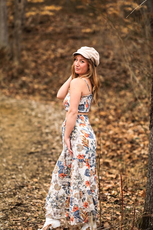 A woman in a floral dress and hat posing in the woods