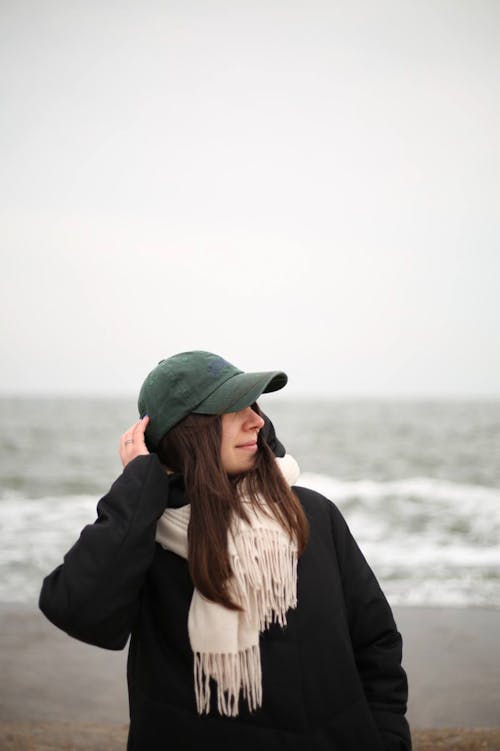 A woman wearing a hat and scarf standing by the ocean